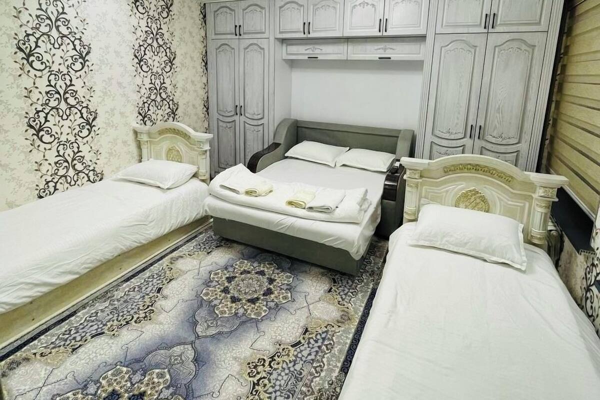 A room with a large bed, two smaller beds, a patterned carpet, and a ceiling light fixture.