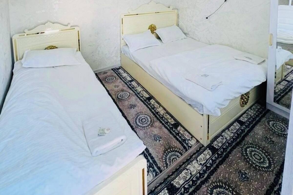 A room with two single beds, a television mounted on the wall, and a patterned rug on the floor.