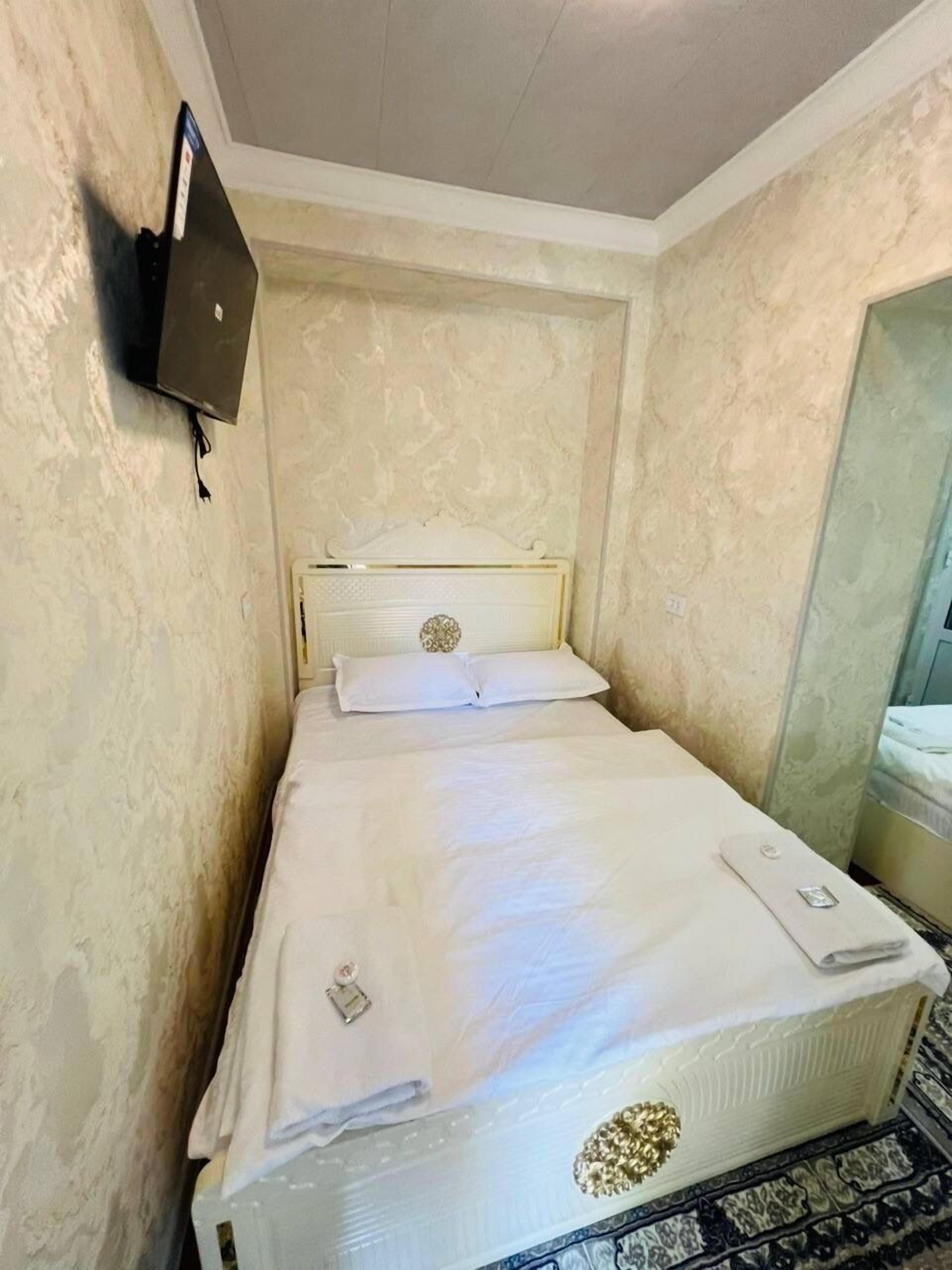 Una habitación de hotel pequeña y estrecha con una cama individual, un televisor en la pared y un espejo.