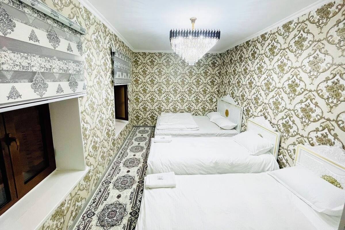 A hotel room with two beds, a chandelier, and patterned wallpaper.