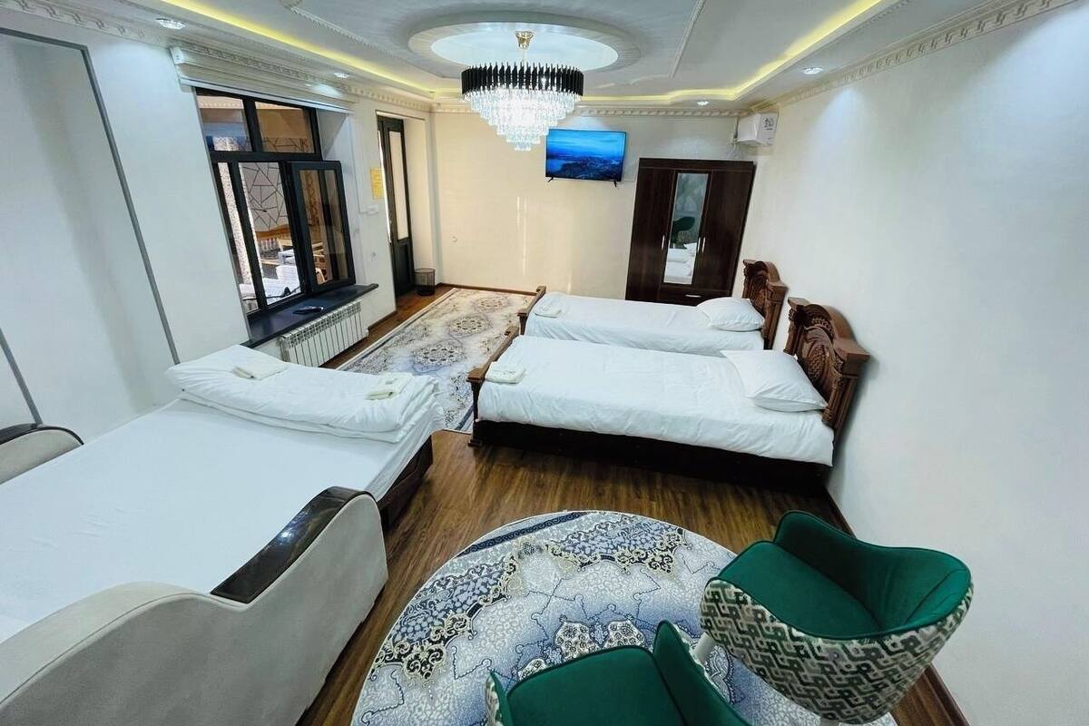 A hotel room with two beds, a television, a chandelier, and a patterned rug.