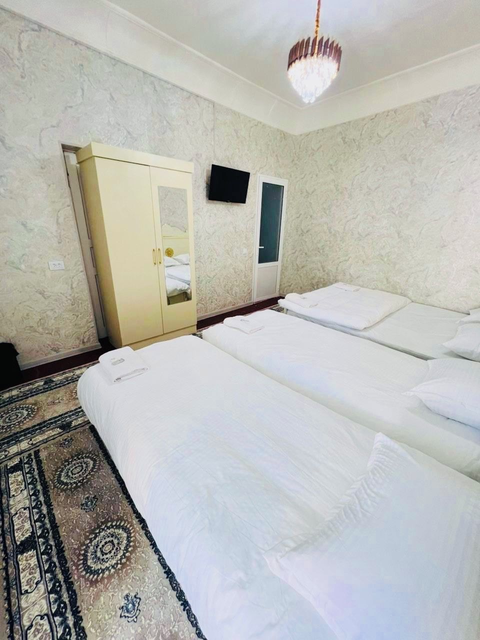 A hotel room with two beds, a wardrobe, a television, and a patterned carpet.