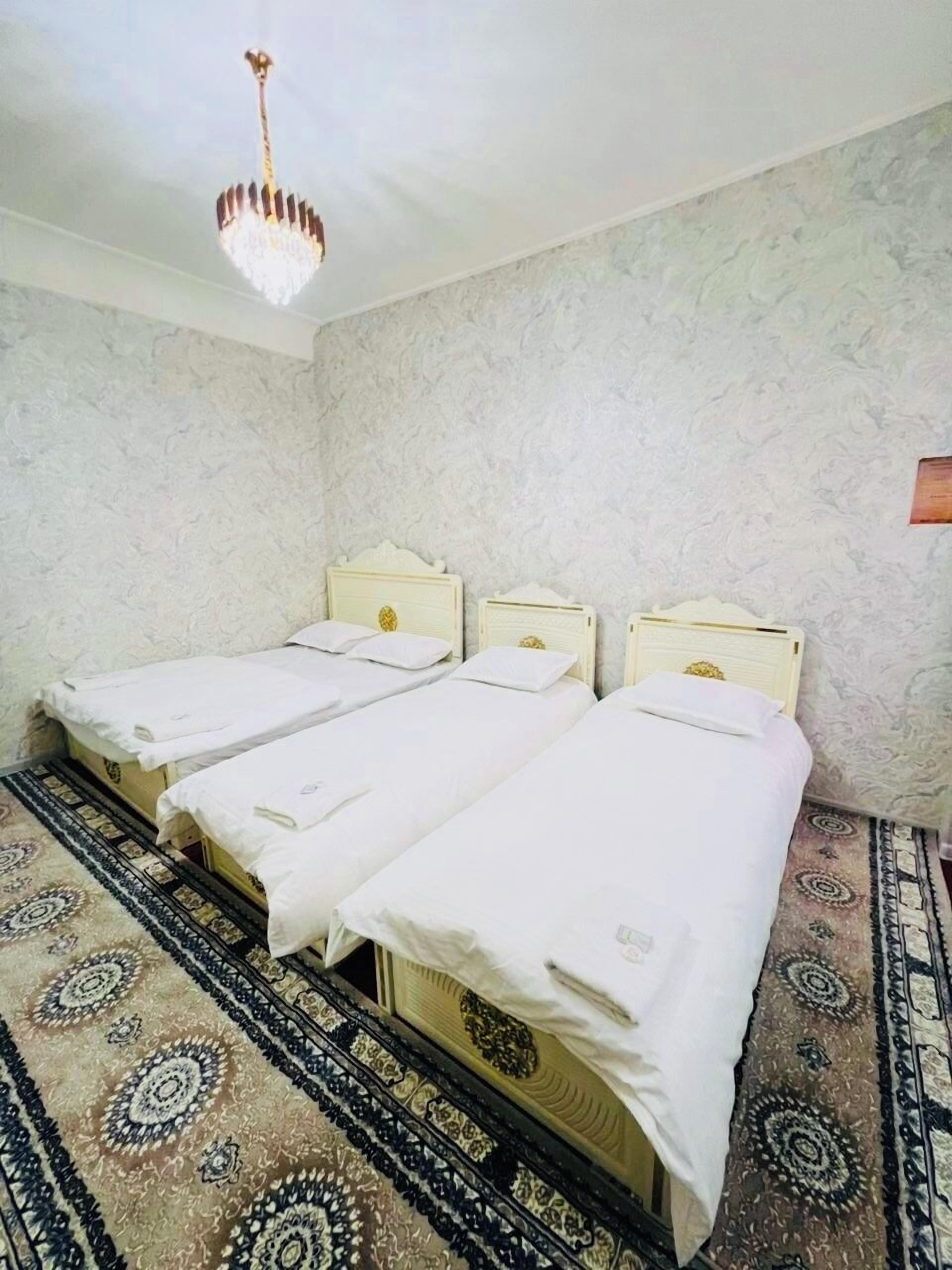 Una habitación con tres camas individuales, una alfombra estampada y un candelabro.