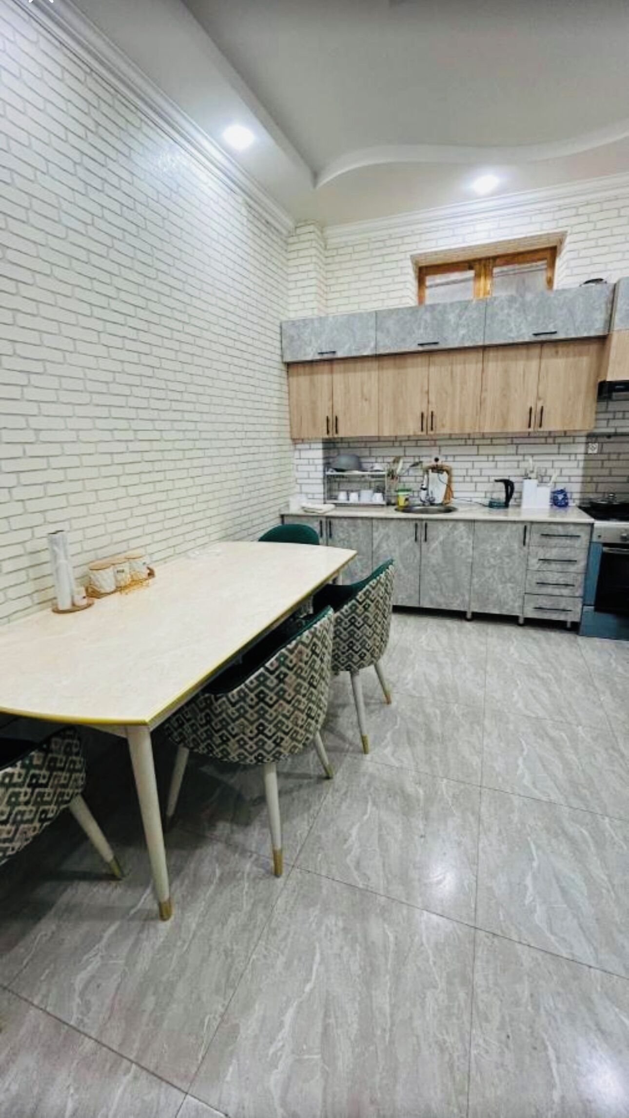 Una cocina moderna con paredes de ladrillo blanco, encimera de mármol y armarios de madera.
