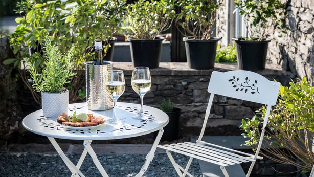 Un bâtiment en pierre avec une table et des chaises de jardin, une bouteille de vin et un verre de vin.