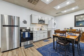 Eine moderne Küche mit Edelstahlgeräten, weißen Schränken, einem Essbereich mit Tisch und Stühlen sowie einem blau gemusterten Teppich.