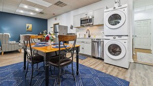 A compact kitchen with a microwave, oven, and washing machine, a dining area with a table and chairs, and a blue rug. - Heron’s Perch - Uptown Port Clinton, Jet Express, 5 minute walk to Beach (Port Clinton)