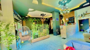 A hotel lobby with a reception desk, seating area, and decorative plants.