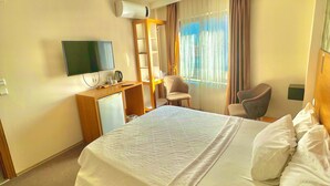 A hotel room with a large bed, a desk with a flat-screen TV, a chair, and a wardrobe.
