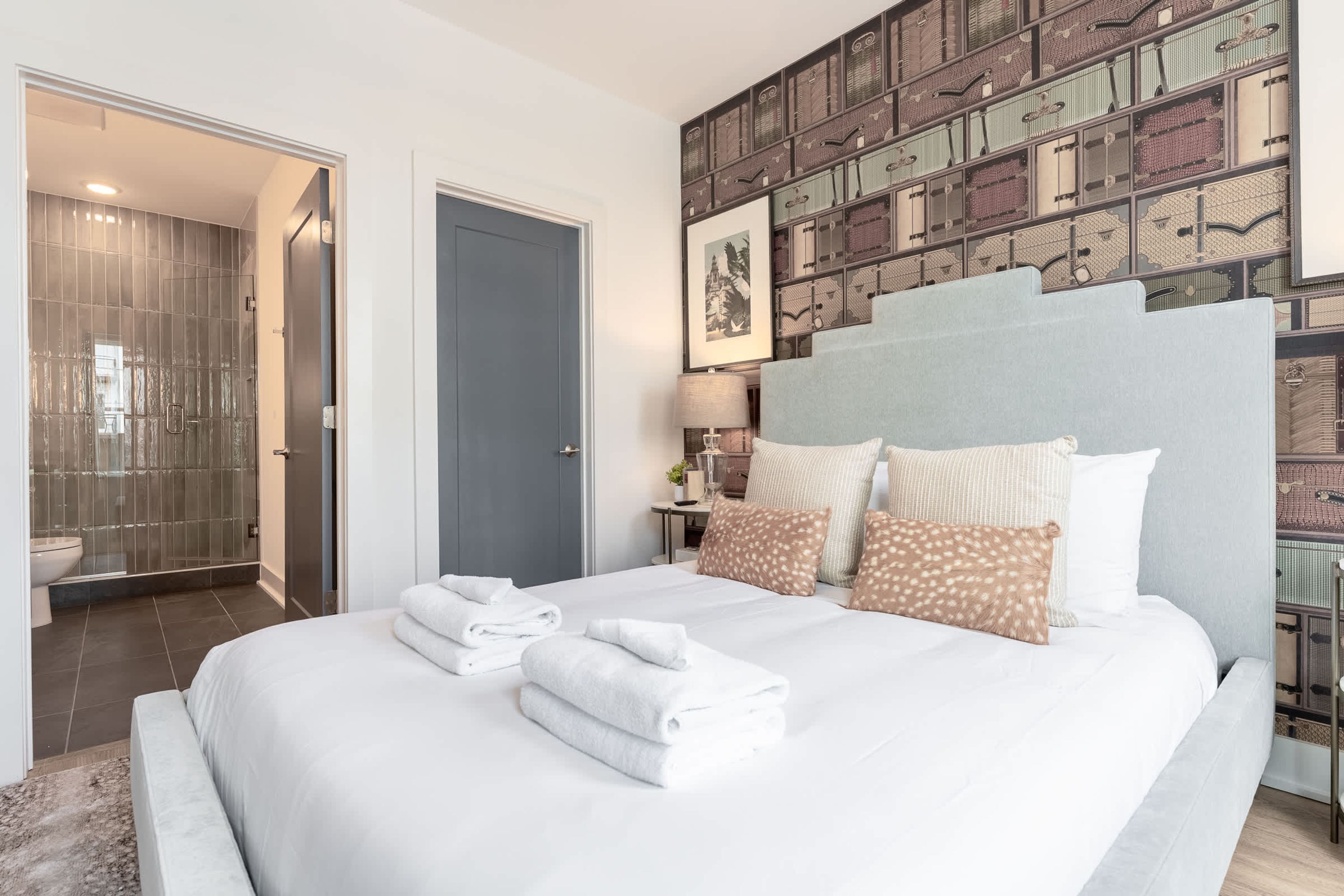 A modern hotel room with a large bed, a shower area, and a wall decorated with vintage suitcases.