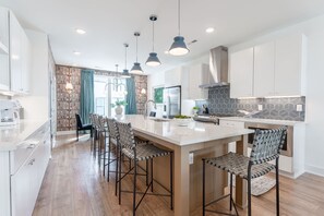 Una cocina moderna con una isla central, taburetes de bar, iluminación colgante y un salpicadero con estampado.