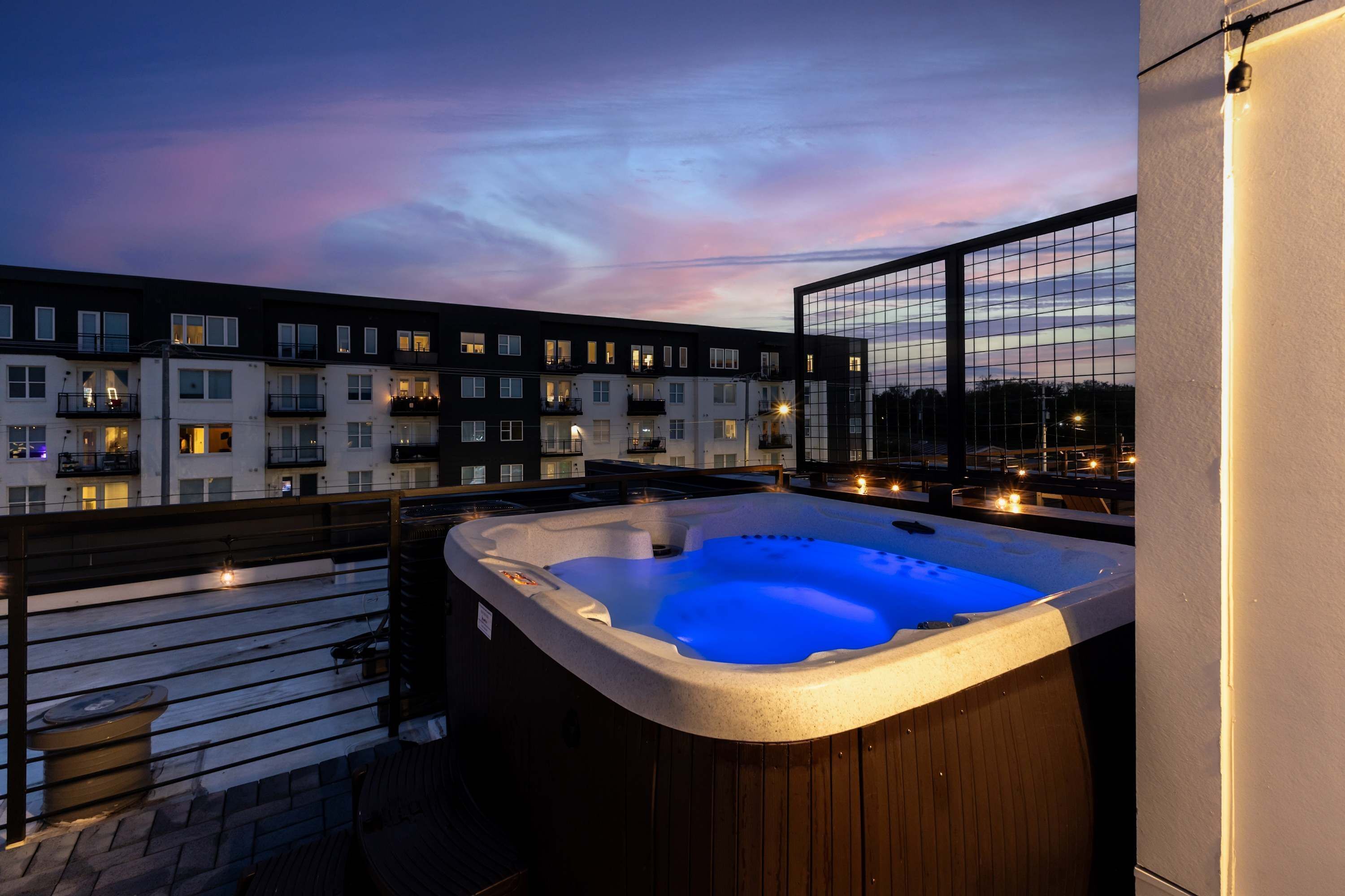 A hot tub on a balcony with a view of a multi-story building at dusk.