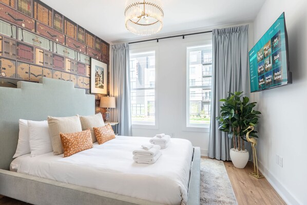Une chambre d’hôtel moderne dotée d’un grand lit, d’un lustre, d’une télévision à écran plat et offrant une vue sur la ville grâce à de grandes fenêtres.
