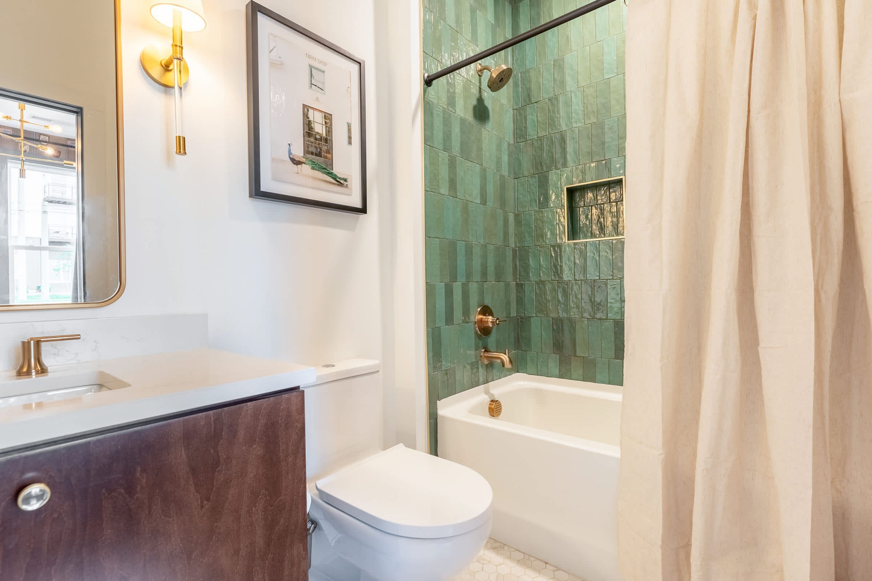 A bathroom with a white sink, a framed picture on the wall, a shower with green tiles, and a white toilet.