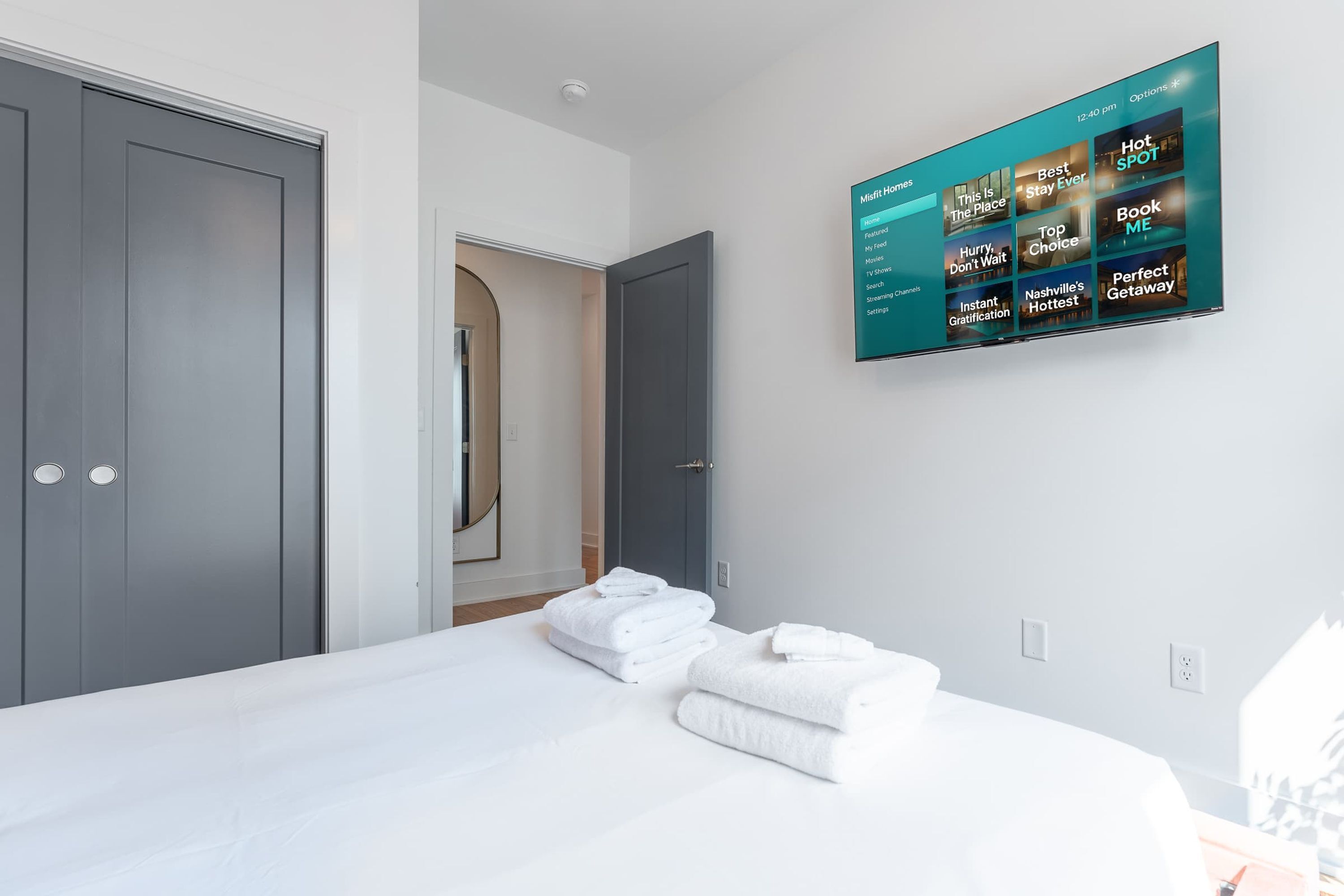 Une chambre d’hôtel équipée d’un lit, d’un téléviseur fixé au mur qui permet d’accéder à différentes chaînes, et d’une porte donnant sur une autre pièce.