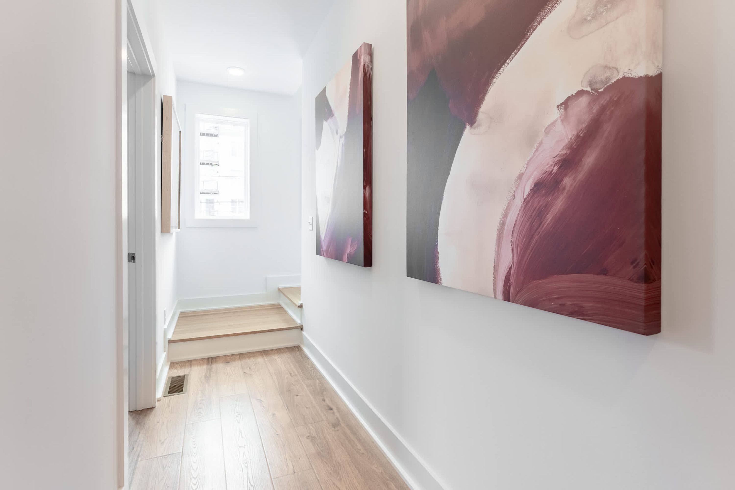 A hallway with wooden flooring, white walls, and two abstract paintings.