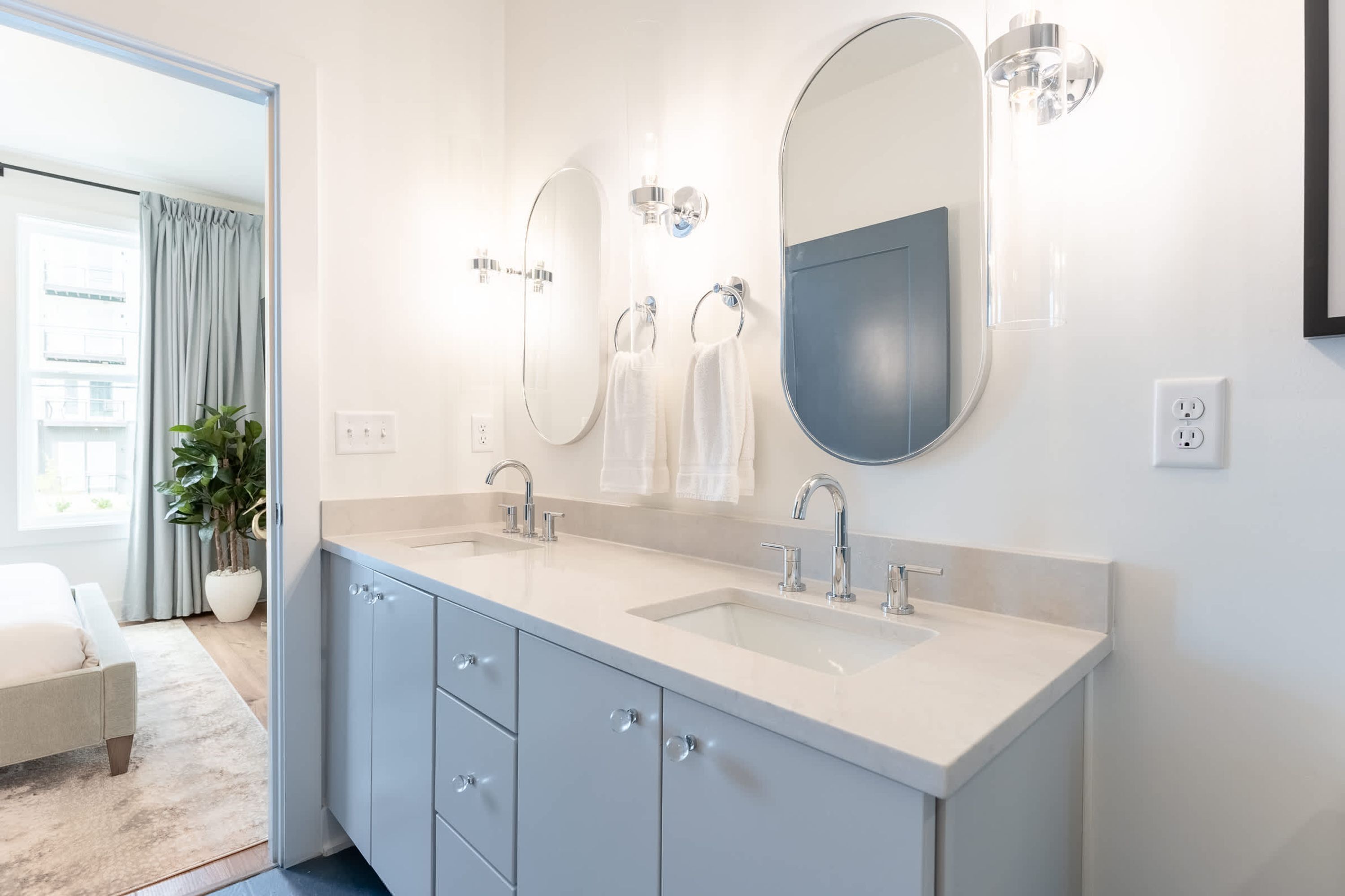 A modern bathroom with two sinks, a large mirror, and a potted plant.