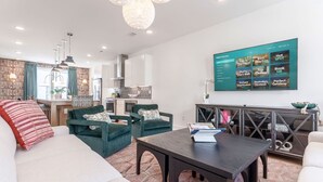 Ein modernes Wohnzimmer mit einer Couch, Sesseln, einem Couchtisch und einem an der Wand montierten Fernseher, der eine Speisekarte zeigt.
