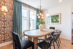Un coin repas avec une table ronde, des chaises noires, une plante en pot et un tableau accroché au mur.