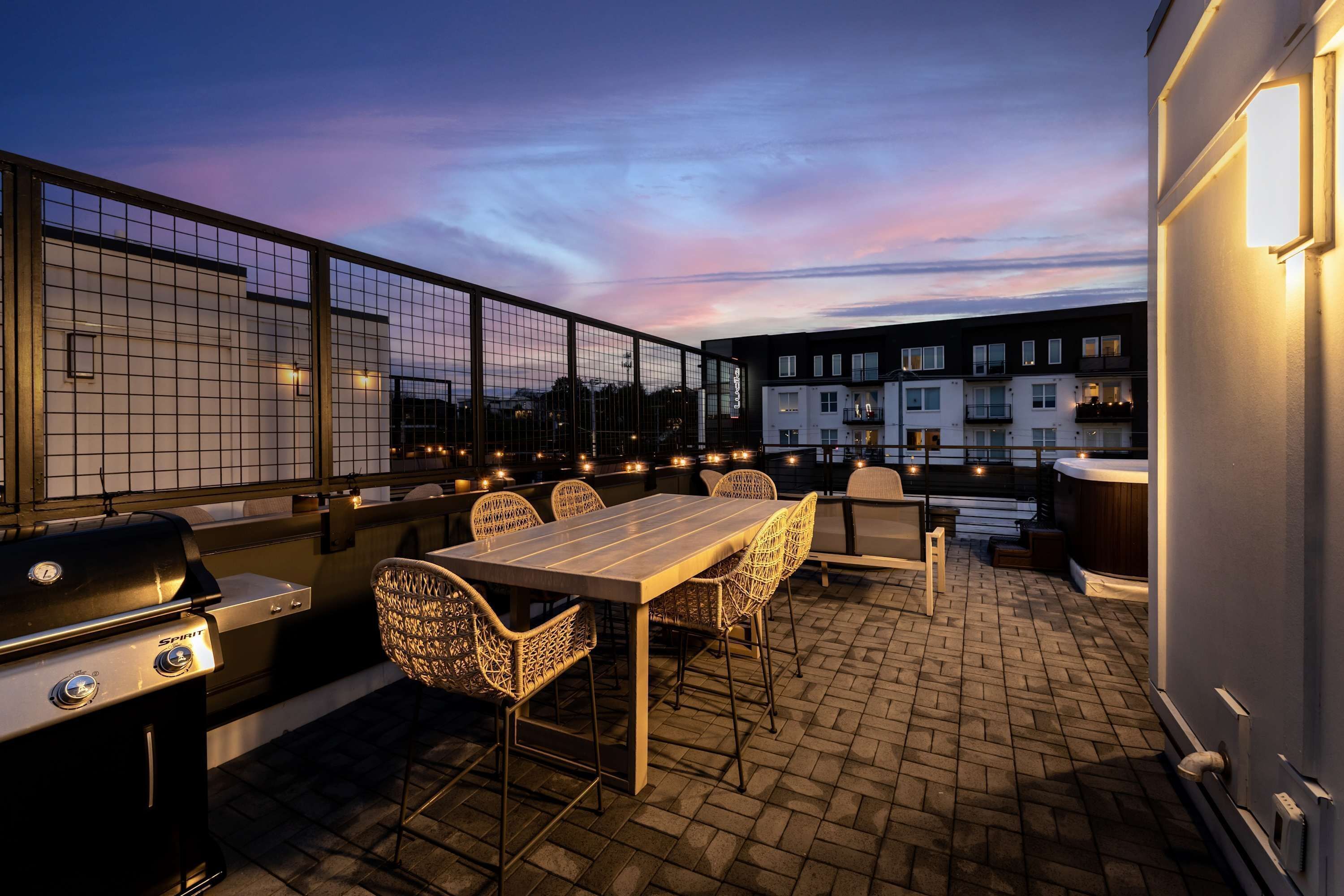 Une terrasse extérieure équipée d’un barbecue, d’une table à manger, de chaises et offrant une vue sur les bâtiments en arrière-plan.