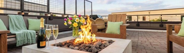 Eine Dachterrasse mit Feuerstelle, Sitzgelegenheiten im Freien und einer Flasche Champagner.