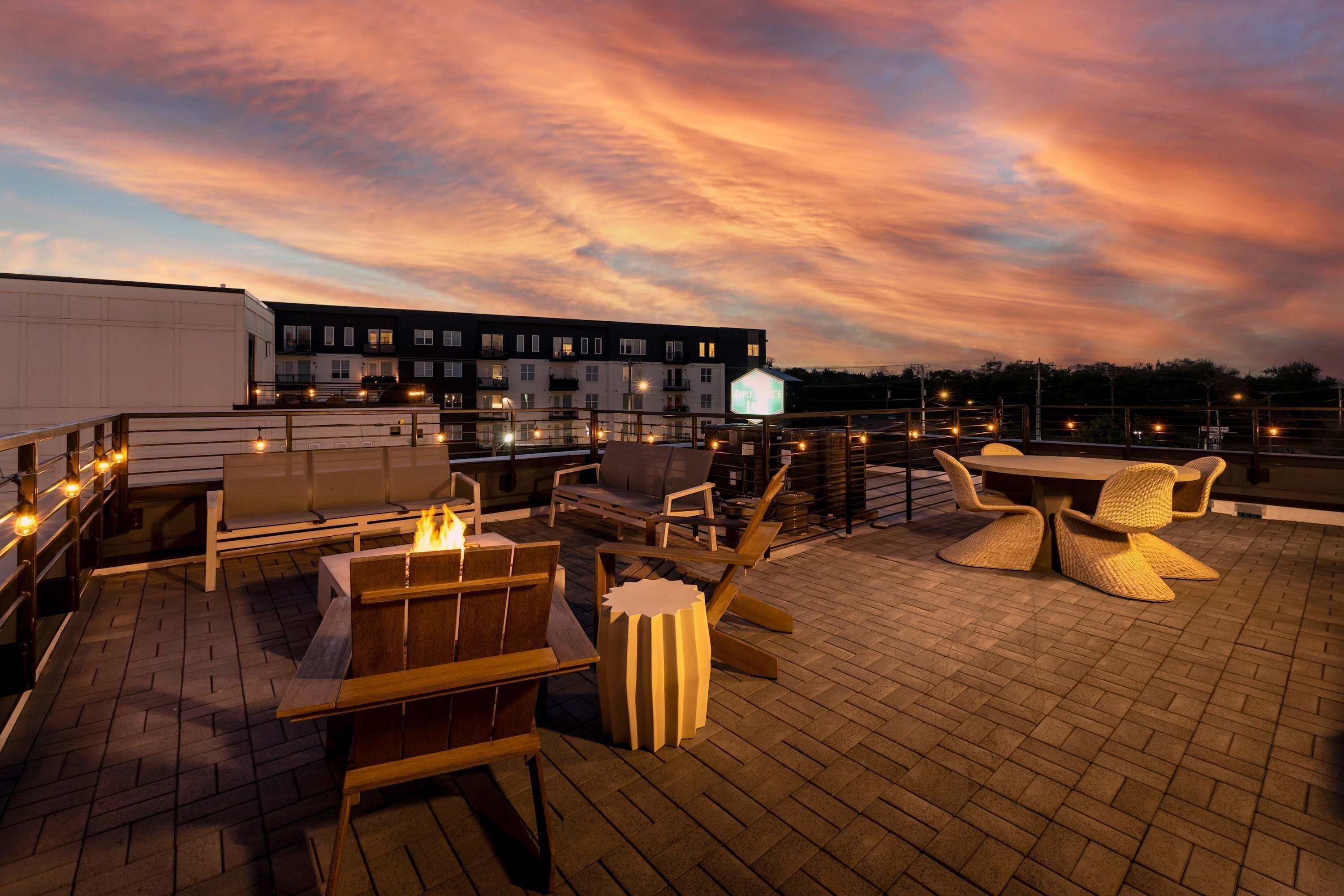 Eine Dachterrasse mit Sitzgelegenheiten im Freien, einer Feuerstelle und Blick auf ein Gebäude im Hintergrund.