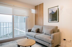 A modern living room with a grey sofa, a wooden coffee table, and a large window with a view of a balcony.