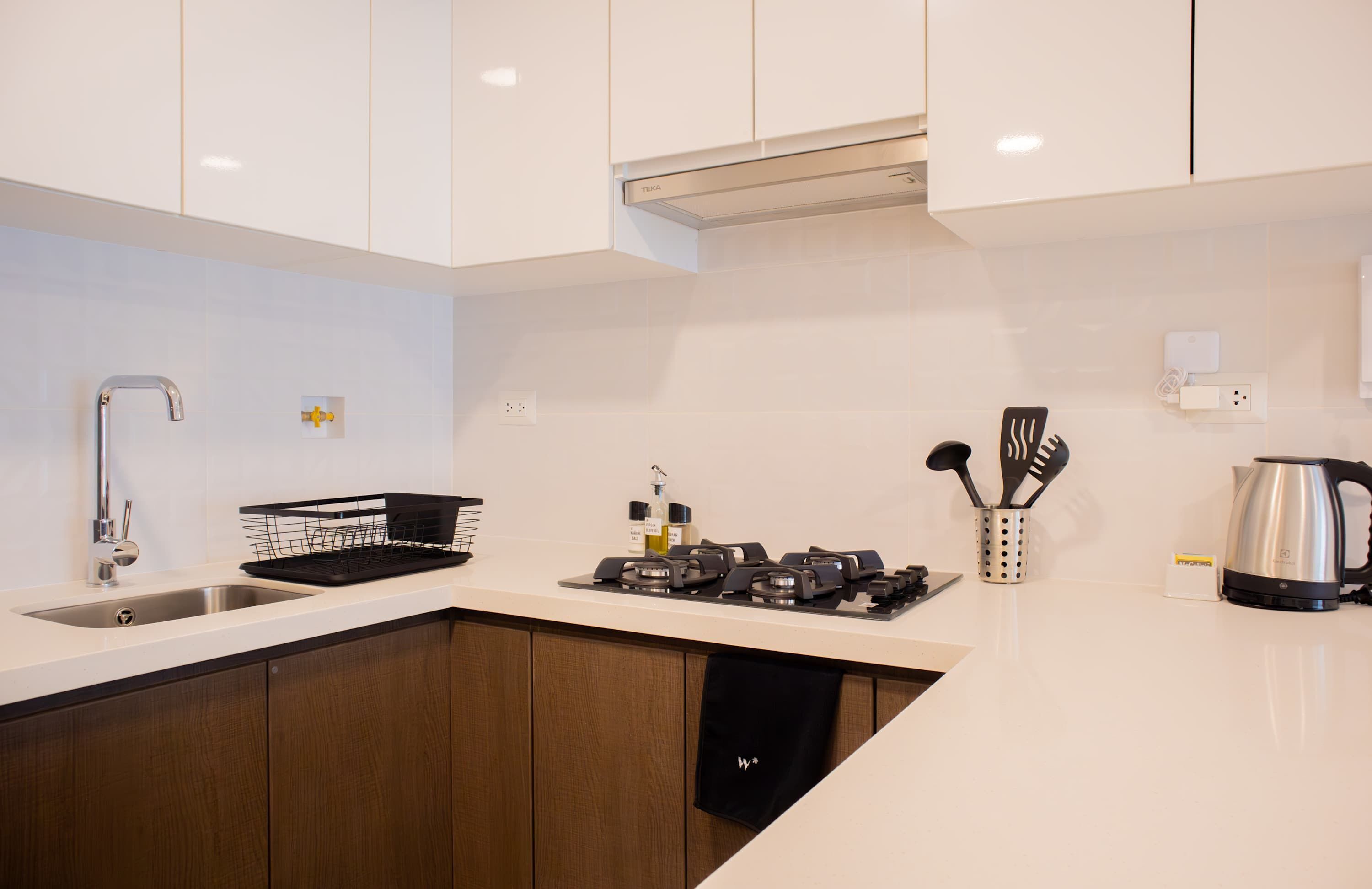 A modern kitchen with white cabinets, a stainless steel sink, a gas stove, and a kettle.