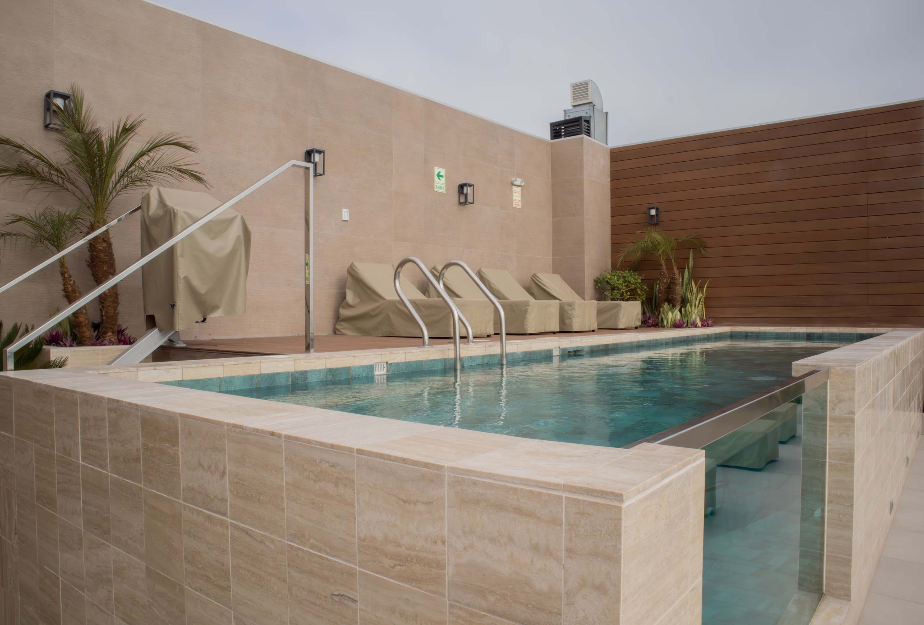 Une piscine avec une terrasse carrelée, un escalier couvert et un climatiseur fixé au mur.