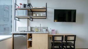 A compact kitchen with a microwave, sink, and a small refrigerator. There is a wooden dining table with two chairs and a flat-screen TV mounted on the wall. - w Peaceful 2BR w Beautiful Terrace in CTG (Cartagena)