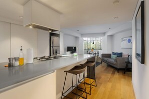 Et moderne køkken med en central ø, barstole, en grå sofa og et spiseområde med stole.