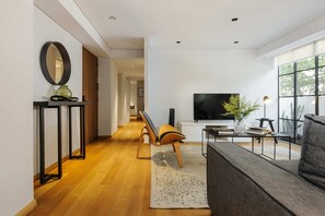 En moderne stue med sofa, fjernsyn, en plante og et konsolbord med et spejl og en vase.