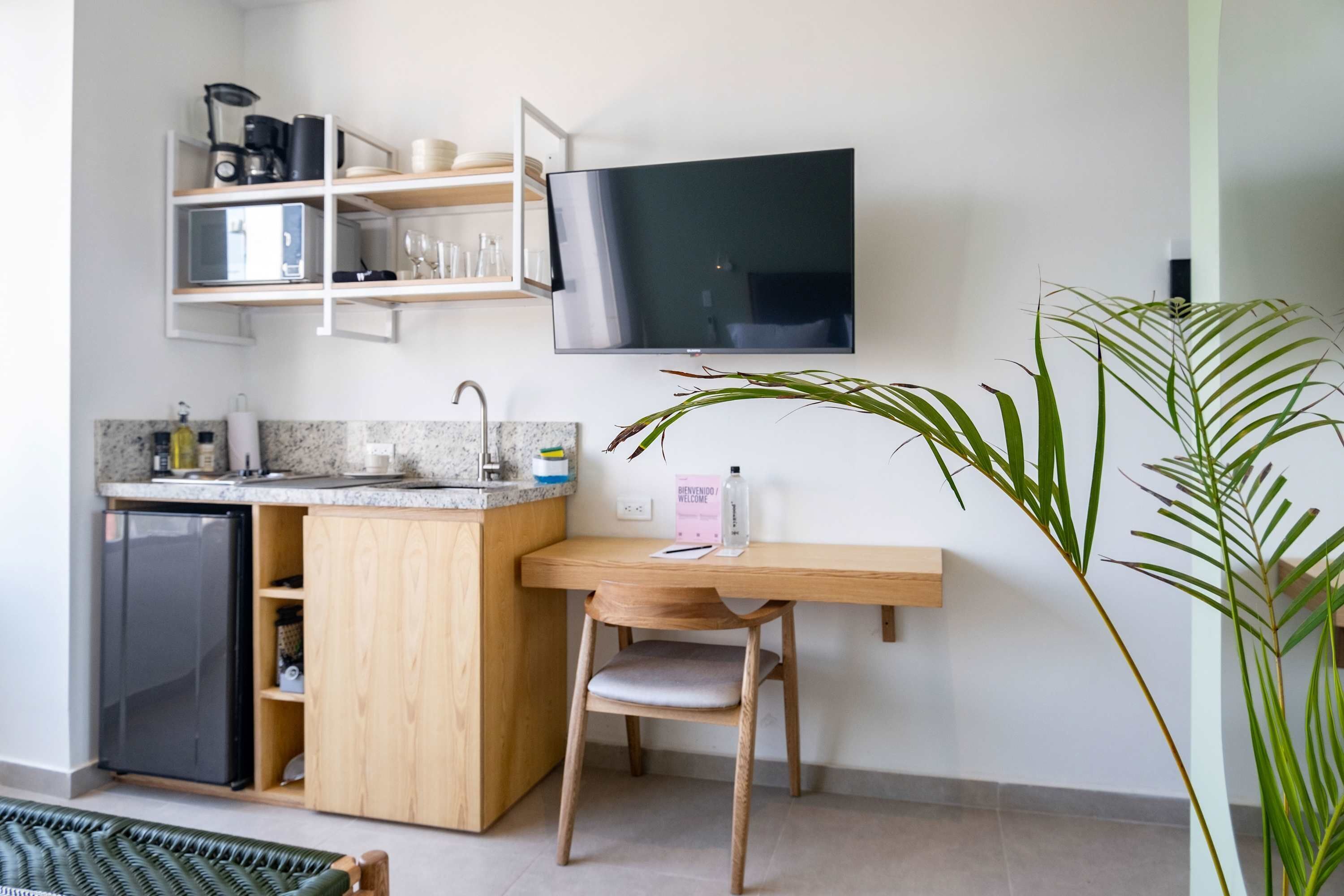 A compact kitchen with a built-in refrigerator, a wooden countertop, a sink, and a wall-mounted TV.