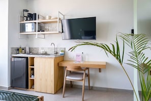 Cocina compacta con refrigerador integrado, encimera de madera, pileta y televisor montado en la pared.