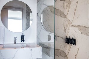 Une salle de bain avec un lavabo en marbre, un miroir rond et une cabine de douche en verre.