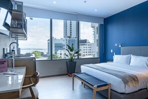 Une chambre d’hôtel moderne avec une grande fenêtre, un lit, un bureau et une plante en pot.