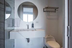 Un baño moderno con tocador de mármol, un espejo redondo, un inodoro y un perchero para toallas.