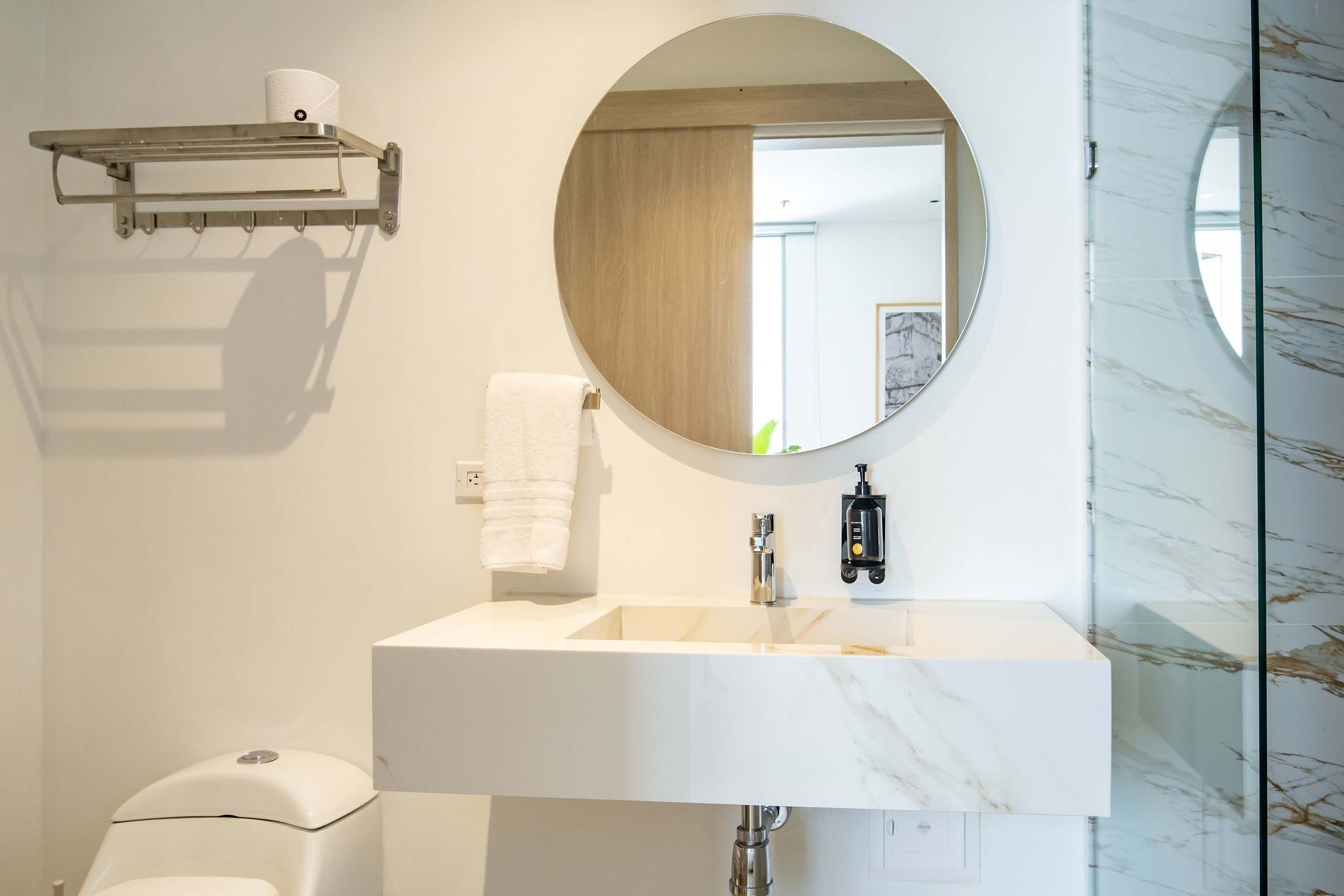 A modern bathroom with a white sink, a round mirror, a towel rack, and a toilet.
