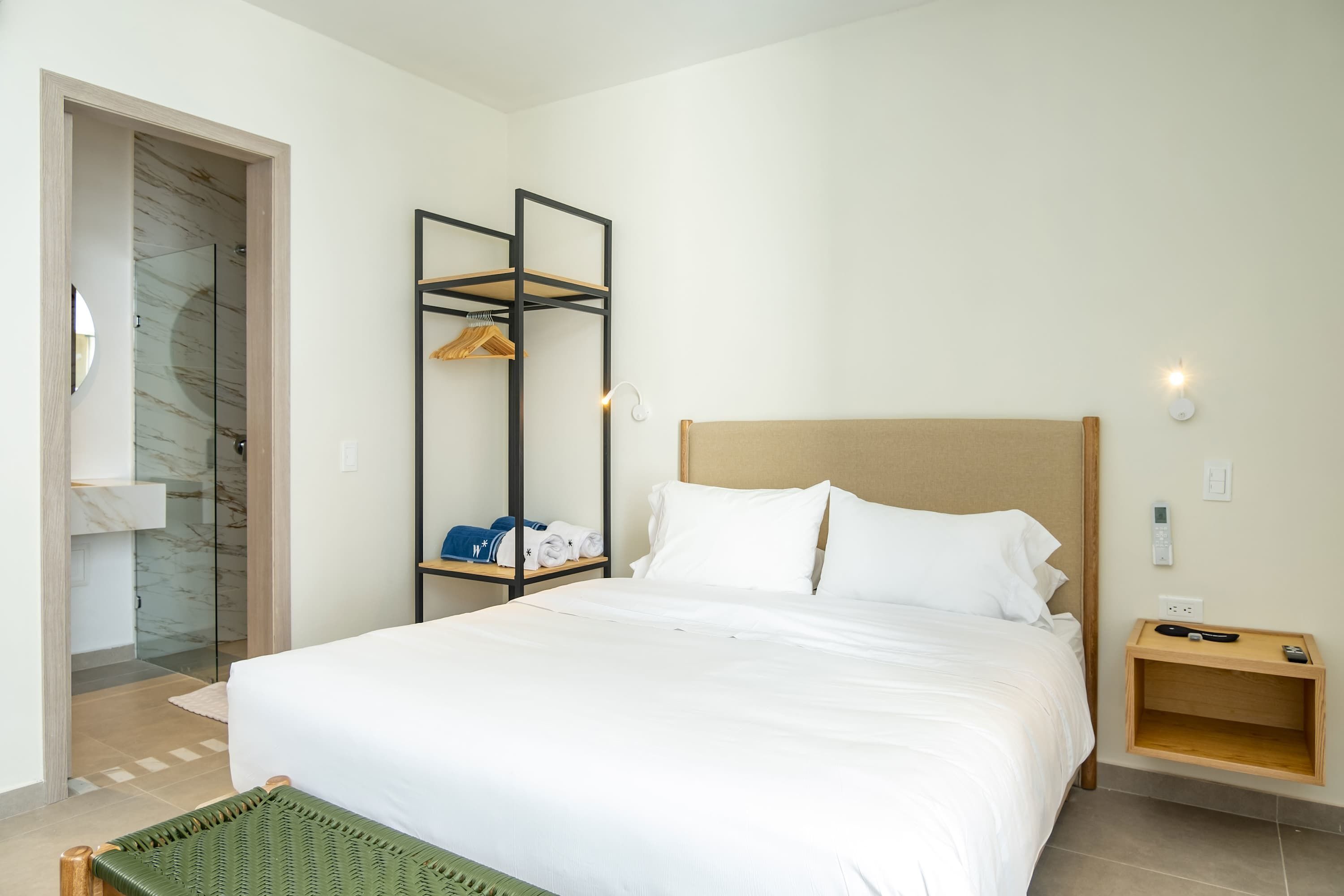A neatly arranged hotel room with a large bed, a wooden nightstand, a built-in wardrobe, and a glass shower enclosure.
