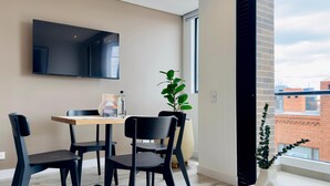 A modern dining area with a wooden table, black chairs, a potted plant, and a TV mounted on the wall. - w Cozy 2BR w Balcony in Santa Barbara (Bogotá)
