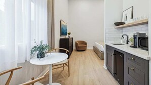 Cozinha moderna com bancada branca, armários escuros e micro-ondas. Possui uma área de refeições com mesa e cadeiras brancas, e uma planta na mesa.