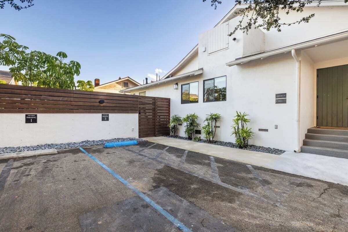 A modern house with a paved driveway, a wooden fence, and a small garden with potted plants.