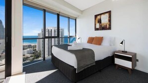 A modern hotel room with a large bed, a nightstand, and a view of the city and ocean. - Sky Lounge 4BR Sub Penthouse (Broadbeach)