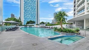 A rooftop swimming pool with lounge chairs, surrounded by modern buildings and greenery. - Sky Lounge 4BR Sub Penthouse (Broadbeach)