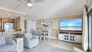 A living room with a TV, seating, and a kitchen area. - Introducing Easy Breezey! 3 BR Gulf Front Listing With A Million Dollar View (Pensacola, FL. 32507)