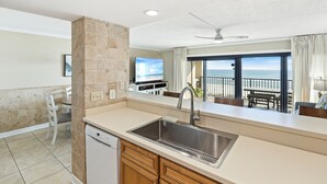 A kitchen with a built-in dishwasher, a stainless steel sink, and a view of the ocean through large windows. - Introducing Easy Breezey! 3 BR Gulf Front Listing With A Million Dollar View (Pensacola, FL. 32507)