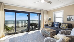 A spacious living room with a large sliding glass door leading to a balcony overlooking the ocean. There is a ceiling fan, a sofa set, and a coffee table. - Introducing Easy Breezey! 3 BR Gulf Front Listing With A Million Dollar View (Pensacola, FL. 32507)