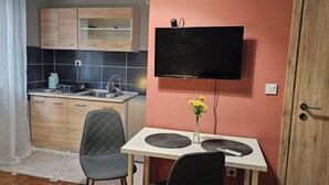 A compact kitchen with a dining area, a TV mounted on the wall, and a door to the right. - KNEZEVIC RESORTS 1
APARTMANI ZA ODMOR I UZIVANJE (Athina)