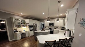 Une cuisine moderne avec des meubles blancs, un grand îlot central doté de tabourets et des appareils électroménagers en acier inoxydable.