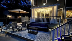 Une terrasse extérieure couverte, aménagée avec des sièges, une table et des guirlandes lumineuses.